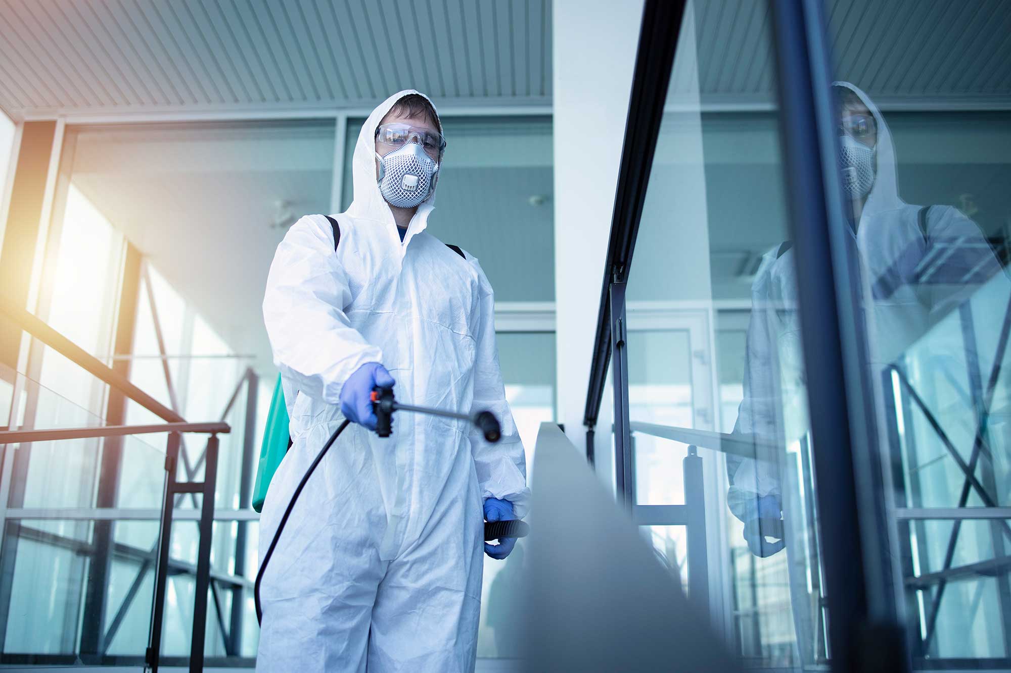 A technician in a protective suit disinfecting a building interior