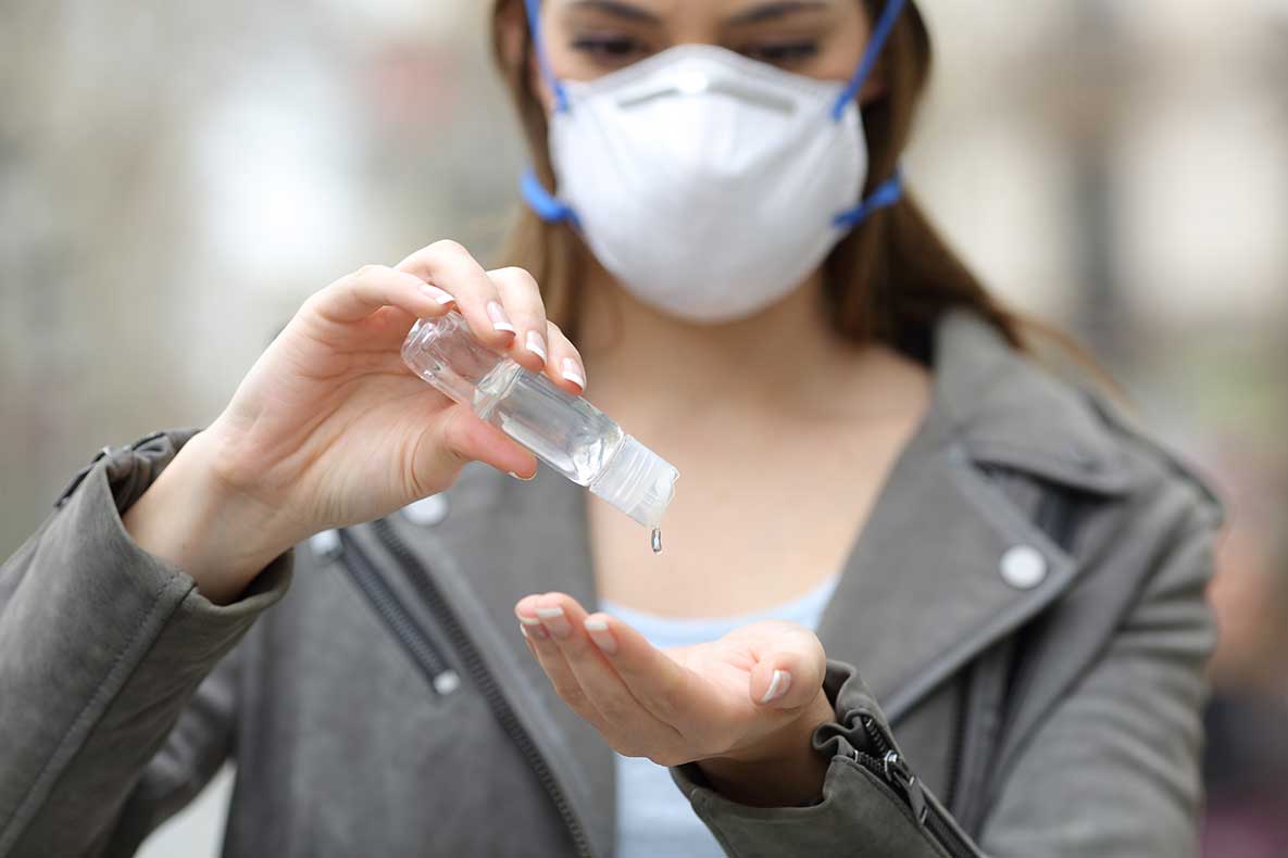 Close up front view of a woman with protective mask using hand sanitizer preventing contagion on street
